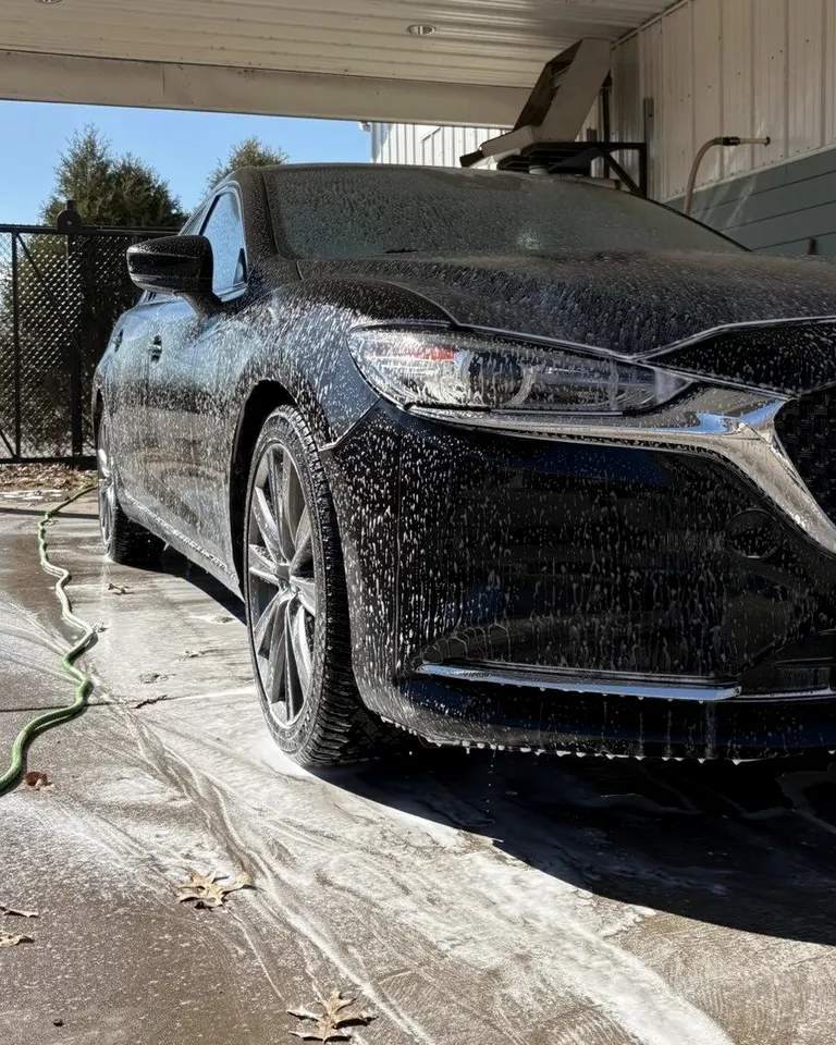 Dark Mazda sedan covered in snow foam under a carport in low sun
