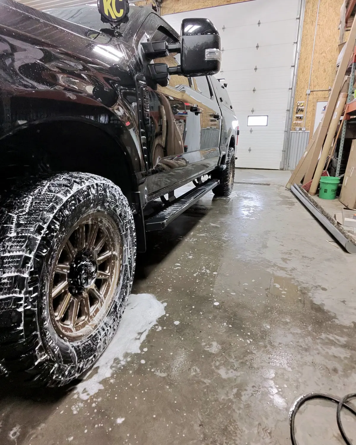 Black Ford Super Duty covered in snow foam inside a garage bay