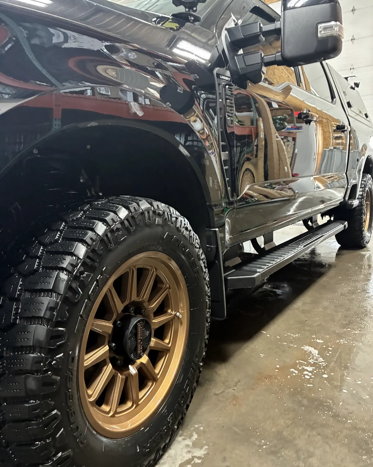 Black Ford Super Duty with bronze wheels, wet and glossy after the rinse inside a garage bay